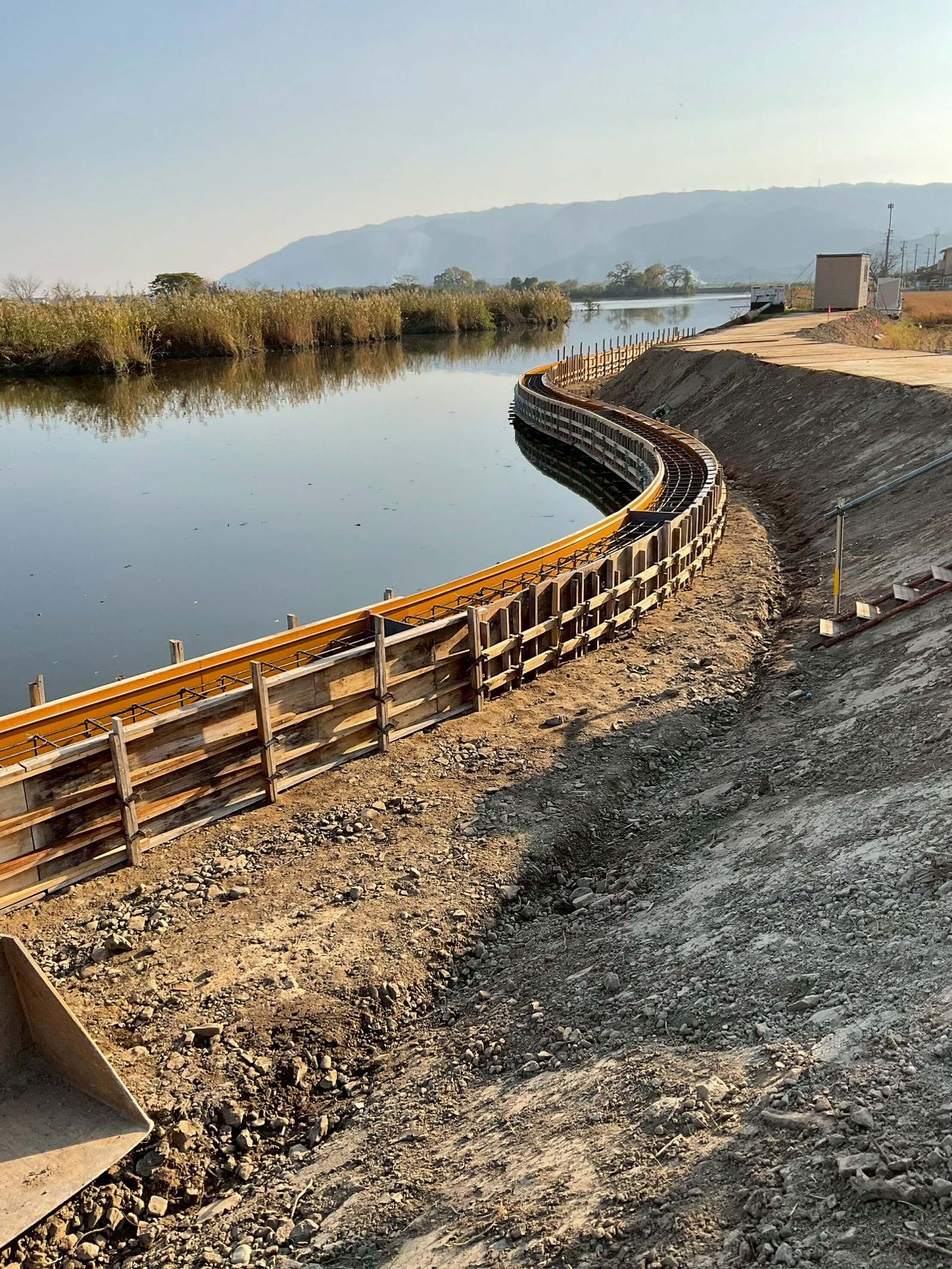 河川沿いの護岸工事で、曲線状に組まれた型枠と鉄筋